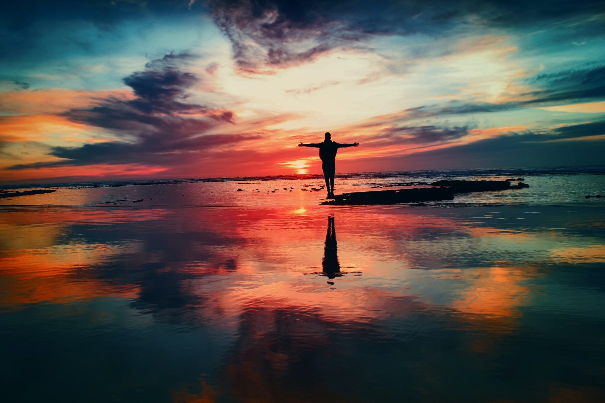 a person facing the sun rise with arms out spread - indicative of a positive attitude