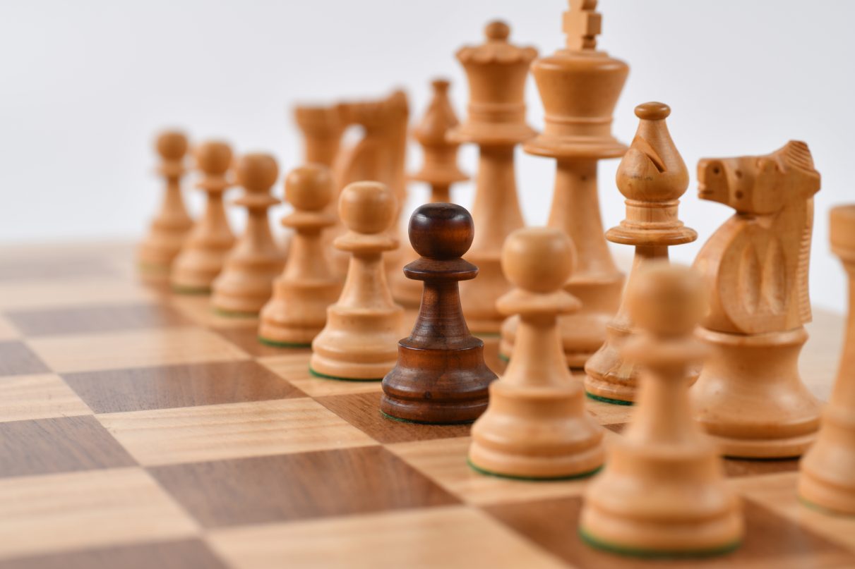 White chess pieces with one black pawn signifying one person having to overcome resistance.