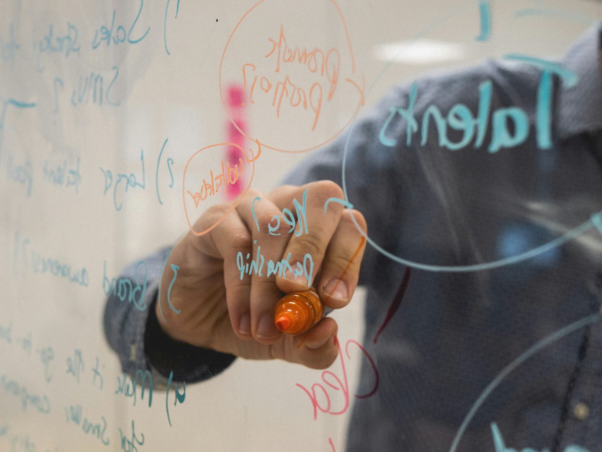 person writing on glass board, making calculations, implying innovation